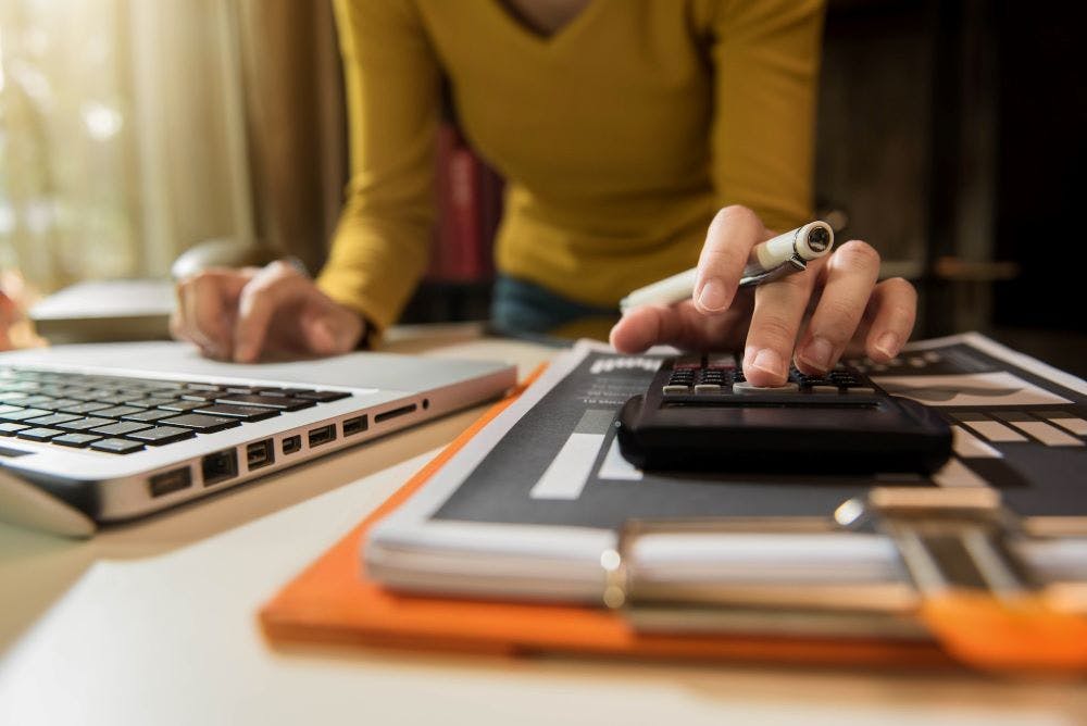 A person performing financial calculations with a laptop and calculator